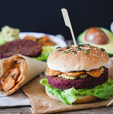 Veg burger di barbabietola rossa e bulghur, con hummus di ceci e avocado, e chips di patata dolce